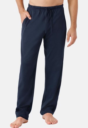 Mann trägt marineblaue Loungehose mit Kordelzug und elastischem Bund, steht barfuß, eine Hand in der Tasche, Bild auf die Taille zugeschnitten.