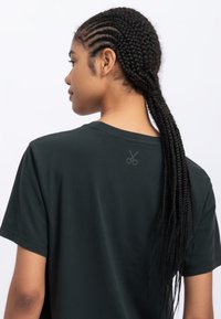 Donkergroene T-shirt met een ronde halslijn en korte mouwen. Kenmerk: kleine schaarafbeelding op de bovenrug. Zachte stof en casual pasvorm.