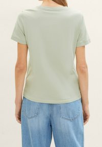Lys grøn t-shirt med korte ærmer og rund halsudskæring. Blød, glat tekstur, skræddersyet pasform og lige kant, parret med blå denimbukser.