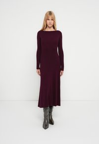 Bourgondische geribbelde gebreide jurk met lange mouwen en een rechte silhouet, reikt tot halverwege de kuit, gecombineerd met grijze kniehoge puntige laarzen.