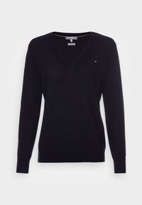 Marinblå V-ringad tröja med långa ärmar, tillverkad av mjukt stickat tyg. Har ribbade muddarna och en liten logotyp på bröstet.