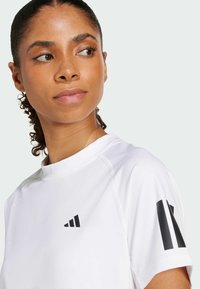 Valge sportlik särk lühikeste varrukatega, ümar väljalõige, mustade logo aktsentidega rinnal ja varrukal. Sile kangastekstuuri.