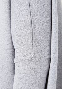 Grauer Sweatshirtstoff mit texturiertem Finish, weiten Bündchen und Nahtdetails am Ärmel. Keine Muster oder zusätzlichen Akzente sichtbar.