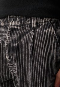 Zwarte corduroy broek met verticale strepen, voorzien van een sluiting met een voorknoop en plooien, met een textuur oppervlak.