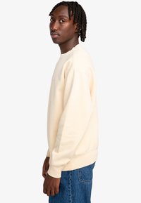 Crème-kleurige sweatshirt met een ronde hals, geribbelde manchetten en tailleband; gedragen met blauwe denim jeans, die een ontspannen pasvorm tonen.