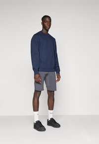 Mørkeblå genser med rund hals, parret med grå shorts. Modellen har på seg sorte sneakers og hvite sokker med merkevare. Enkelt design.