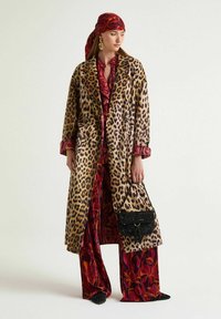 Cappotto con stampa leopardata dalla silhouette oversize, abbinato a una maglia rossa con motivo floreale e pantaloni a gamba larga. Accessoriato con una borsa nera testurizzata.