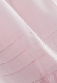 Weicher rosa Stoff mit horizontalen abgesteppten Falten, die eine geschichtete Textur und sanfte Falten erzeugen.