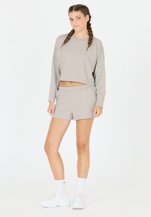 Ljusgrå skaftpullover med långa ärmar och matchande shorts. Mjukt tyg, avslappnad passform, i kombination med vita träningsskor och strumpor.