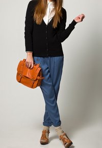 Svart knapp-up kofta över en vit skjorta, ljusblå byxor, beige läderskor och en orange handväska med hårdvaru detaljer.