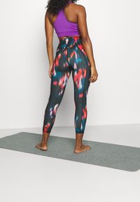 Leggings med svart bas, prydda med en färgglad abstraherad design i rött, blått och vitt. Kombinerat med en lila crop top.