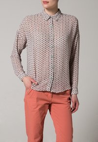 Camicia a maniche lunghe con bottoni, di base rosa chiaro, caratterizzata da piccoli motivi a cuori multicolori e bottoni verdi; abbinata a pantaloni corallo.