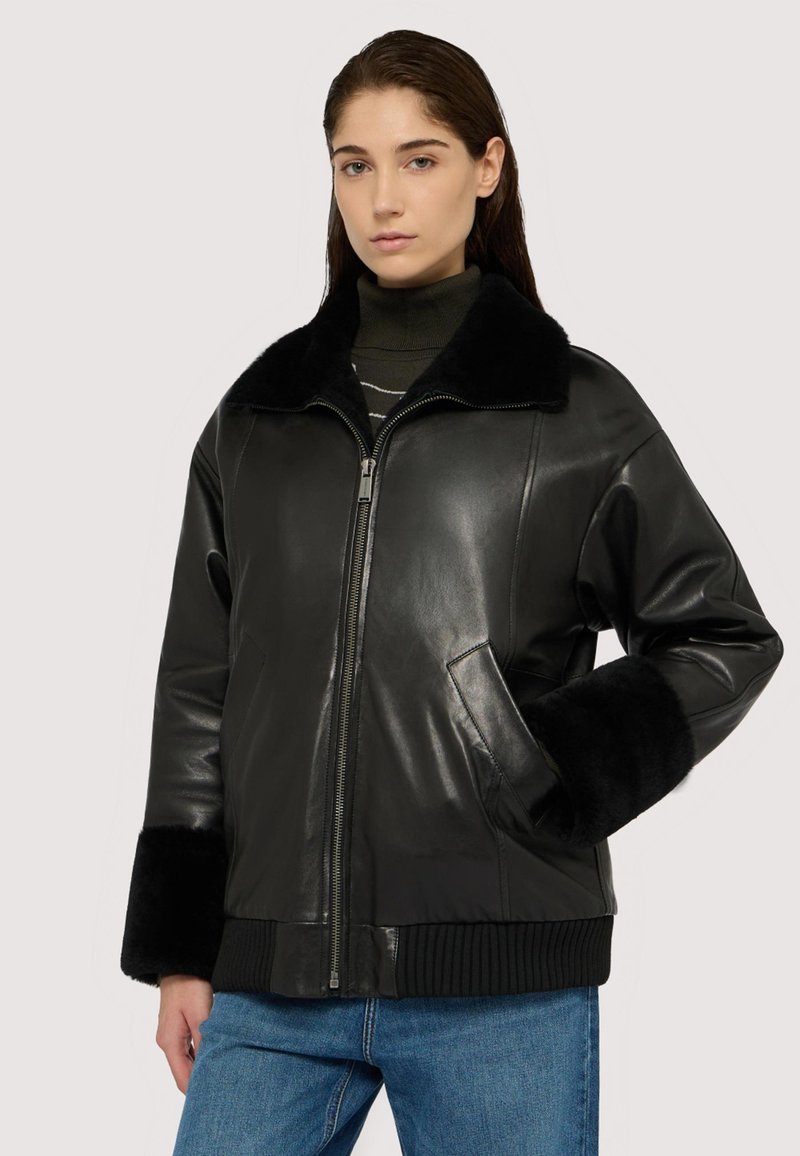 Czarna skórzana kurtka z futrzanym kołnierzem, na zamek błyskawiczny i ściągaczami przy mankietach. Ma boczne kieszenie i luźny krój, zestawiona z niebieskimi dżinsami.