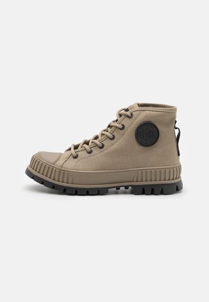 Botte montante en toile kaki avec semelle en caoutchouc, bout rond, laçage à l'avant et patch logo circulaire noir sur le côté.