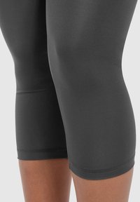 Leggings neri fino al ginocchio realizzati in tessuto elastico, con una superficie liscia e cuciture rinforzate all'orlo.