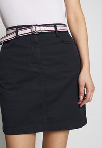 Zwarte katoenen rok met een nauwsluitend ontwerp en riemlussen. Voorzien van een rood-wit-blauw gestreepte riem met een zilveren gesp.