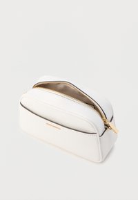 Valkoinen nahkainen kosmetiikkapussi, jossa on kultainen vetoketju, pyöreä muoto, sileä pinta ja hillitty brändin nimi kohopainettuna etupuolella.