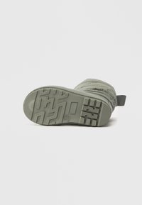 Semelle de botte verte en caoutchouc texturé pour une bonne adhérence, avec un motif en zigzag et une languette pour faciliter l'enfilage.