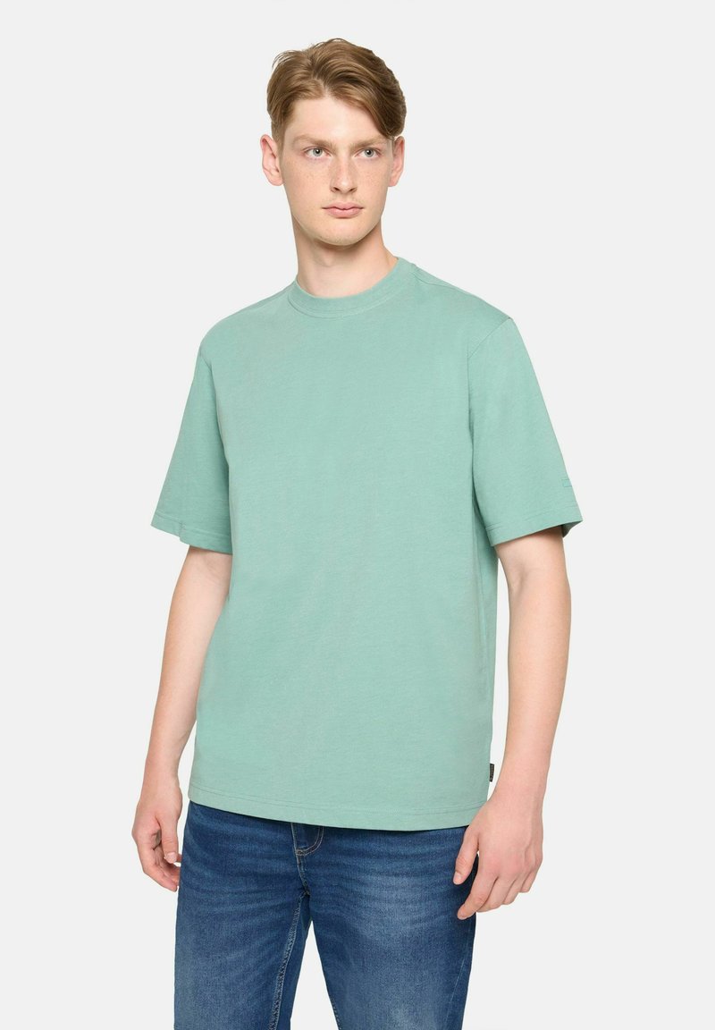 Tricou din bumbac de culoare verde mentă, cu guler rotund și mâneci scurte, având o croială lejeră și o textură subtilă. Purtați cu blugi albaștri.