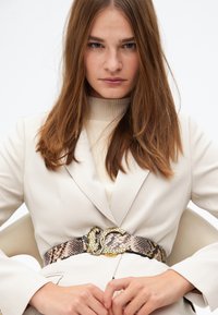 Bälte med en spänne i ormdesign, tillverkat av läder med ormtryck i bruna nyanser och guldaccenter.