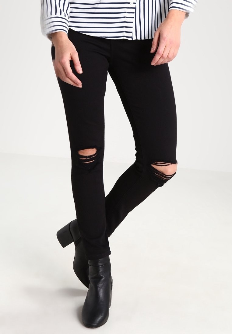 Černé roztrhané džíny s úzkým střihem, s vybledlými oblastmi na kolenou. Spárovány s černými kotníkovými botami na podpatku a bílou pruhovanou košilí s dlouhým rukávem.