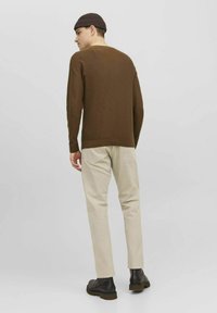 Pull marron côtelé avec un col rond, associé à un pantalon beige clair et des bottes noires. Le pull a des manches longues et une coupe décontractée.