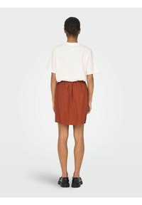 T-shirt bianco a maniche corte abbinato a una gonna elastica arancione-marrone, disponibile con scarpe nere chunky, mostrato da dietro.
