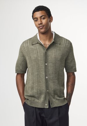Short-sleeve green knit shirt with vertical textured stripes, collar, and buttons. Worn over a white undershirt with a relaxed fit.
