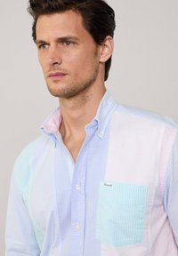 Overhemd met knopen in pastelkleuren: lichtblauw, roze en wit. Gestreept patroon met een opgestikte zak en contrasterende kraagdetails.