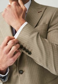 Hellbrauner, schmal geschnittener Anzugjacke mit Nadelstreifen. Sie verfügt über vier dunkle Knöpfe an den Ärmeln und ein kontrastierendes weißes Hemd darunter.