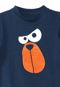 Himmelblaues Baumwoll-T-Shirt mit einer großen, orangefarbenen Hundegesicht-Applikation mit weißen Augen und einer strukturierten Nase, rundem Halsausschnitt und kurzen Ärmeln.