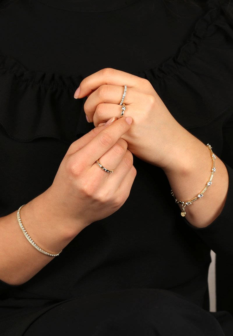 Tre smycken: ett silverarmband, ett guldarmband med små stenar, och två ringar, en guld- och en silversmycke med ädelstenar, bärs på händerna.