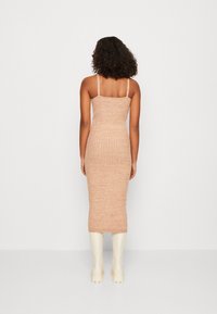 Robe midi en tricot beige avec une silhouette ajustée, des bretelles fines et un motif texturé, portée avec des bottes blanches jusqu'aux genoux.