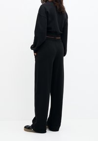 Schwarzes, verkürztes Sweatshirt mit überschnittenen Schultern, kombiniert mit locker sitzenden schwarzen Jogginghosen mit elastischem Bund und seitlichen Taschen.