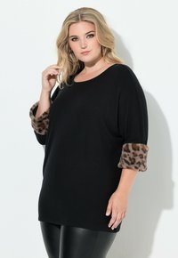 Czarny luźny sweter z leopardzim nadrukiem na sztucznych futrzanych mankietach. Miękka tekstura, szeroki dekolt i rękawy do ćwierć długości. Połączony z błyszczącymi czarnymi legginsami.