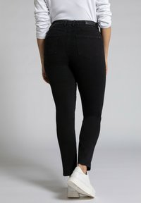 Black denim jeans with a high waist, slim fit, featuring two back pockets and a smooth texture. Worn with white sneakers.