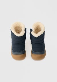 Tengerészkék téli csizmák barna gumitalpakkal és puha, krémszínű műszőrme béléssel, felülről nézve fehér háttér előtt.