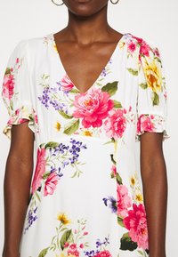 Blommig klänning med V-ringning, korta puffärmar och vit bakgrund. Har rosa, lila och gula blommönster. Mjuk textur.