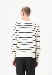 Sweater riscado em creme com riscas pretas, punhos e bainha canelados, gola redonda, textura malha e detalhes de botões no ombro.