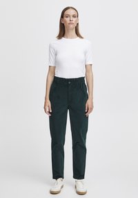 Dark green, textured, loose-fitting pants with an elastic waistband and side pockets, paired with a fitted white short-sleeve top.