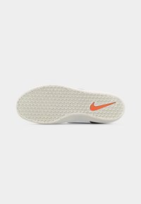 Valge kummist jalanõu tall, millel on tekstureeritud haardemuster ja oranž Nike Swooshi logo kanna lähedal tavalisel taustal.