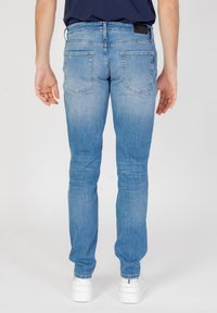 Jeans de mezclilla azul deslavados con un ajuste ajustado, que presentan dos bolsillos traseros, un sutil patrón de lavado y una etiqueta negra en la cinturilla. Zapatillas blancas visibles.