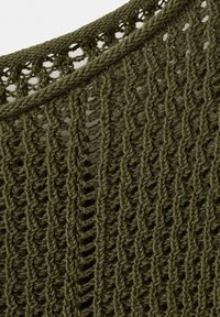 Nærbillede af olivengrønt strikket stof med vertikalt åbent stingmønster og tekstureret flettet halsudskæring.