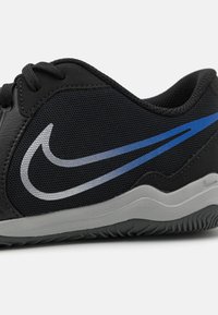 Zapatilla deportiva negra que combina materiales de malla y cuero, con un detalle del swoosh de Nike en gris y azul, suela de goma texturizada y diseño curvado.