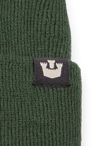 Knit green beanie featuring a black label with a white castle graphic. The fabric texture is ribbed and the design is simple and functional.