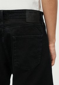 Κοντινή εικόνα της πίσω τσέπης και της μέσης μαύρου τζιν από τζιν με ετικέτα δέρματος Jack & Jones στη δεξιά πλευρά.