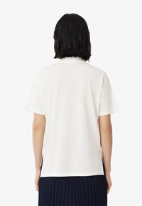 Vit kortärmad t-shirt med en mjuk textur och klassisk krage. Har sidslitsar för bättre rörlighet och bärs med en veckad marinblå kjol.