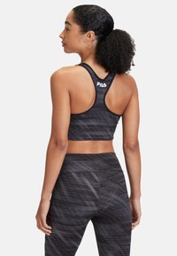 Schwarzes sportliches Crop-Top mit Racerback-Design. Verfügt über ein strukturiertes Muster und ein weißes FILA-Logo auf der Rückseite. In Kombination mit passenden gemusterten Leggings.