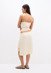 Camisola de culoare crem cu bretele subțiri și o fustă asortată. Ambele au accente din dantelă și o fante. Material neted, ușor.