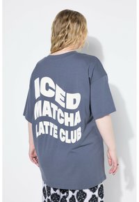 Šedé oversize tričko s velkým bílým nápisem "ICED MATCHA LATTE CLUB" na zadní straně. Měkký materiál, krátké rukávy, volný střih.